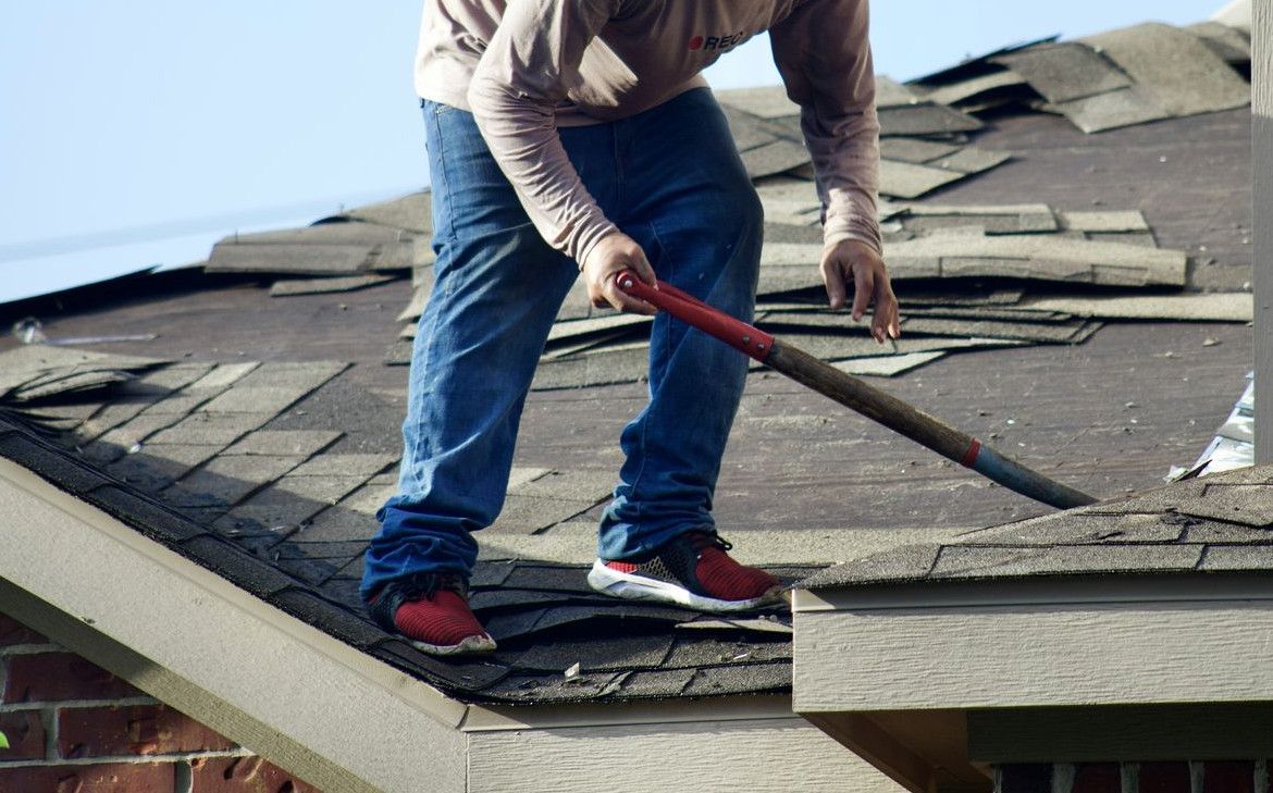 A person in a long-sleeved shirt removing shingles from a residential roof